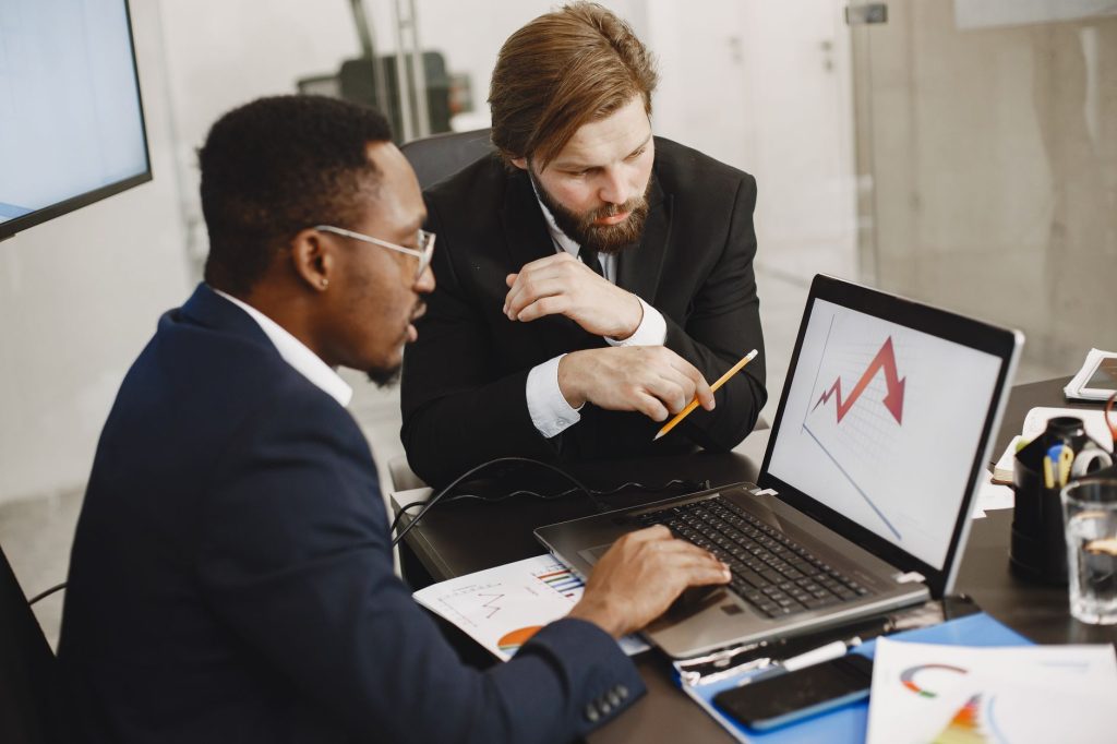 Two business professionals discuss marketing data on a laptop in a modern office. — "Financial Independence with Flexibility:
