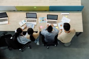 Aerial view of four colleagues working with laptops and documents at a shared desk. — How can business individuals gain benef