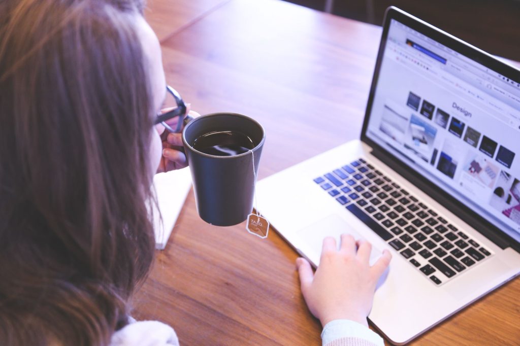 A woman enjoys coffee while browsing the web on a laptop at a home office desk. — How to Prevent Internet Throttling