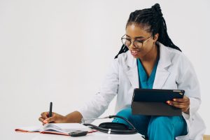 Smiling female doctor in scrubs using tablet and taking notes in a healthcare setting. — How Virtual TRT Clinics Provide Flex