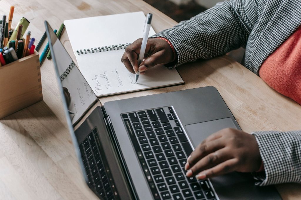 Crop unrecognizable African American female in formal wear writing notes in notepad while working on laptop — Peru TEFL: Not