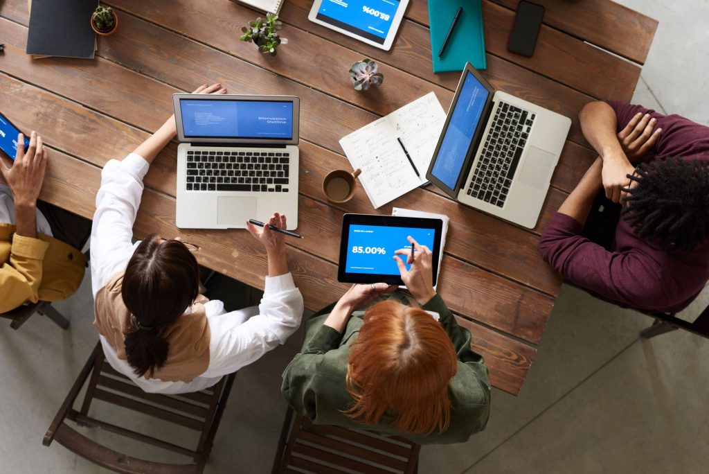 Team discussing strategies around a wooden table with laptops and tablets. — Reasons Why Your SEO Strategy Is Not Working