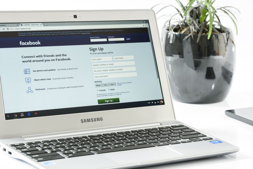 Open Samsung laptop showing Facebook sign-up page next to a potted plant. Ideal for technology themes. — Social Internet Mark