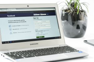 Open Samsung laptop showing Facebook sign-up page next to a potted plant. Ideal for technology themes. — Social Internet Mark