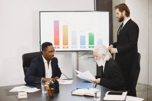 Three businessmen discussing financial data in a modern office setting with charts. — A Must For Your Financial Futur