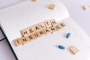 Close-up of health insurance spelled out with Scrabble tiles on a planner, alongside medication pills. — Stuart Piltch Champi