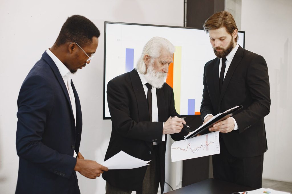 Three businessmen in suits reviewing reports and graphs during an office meeting. — The Best Way to Change Your PDFs into Mic