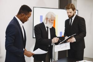 Three businessmen in suits reviewing reports and graphs during an office meeting. — The Best Way to Change Your PDFs into Mic