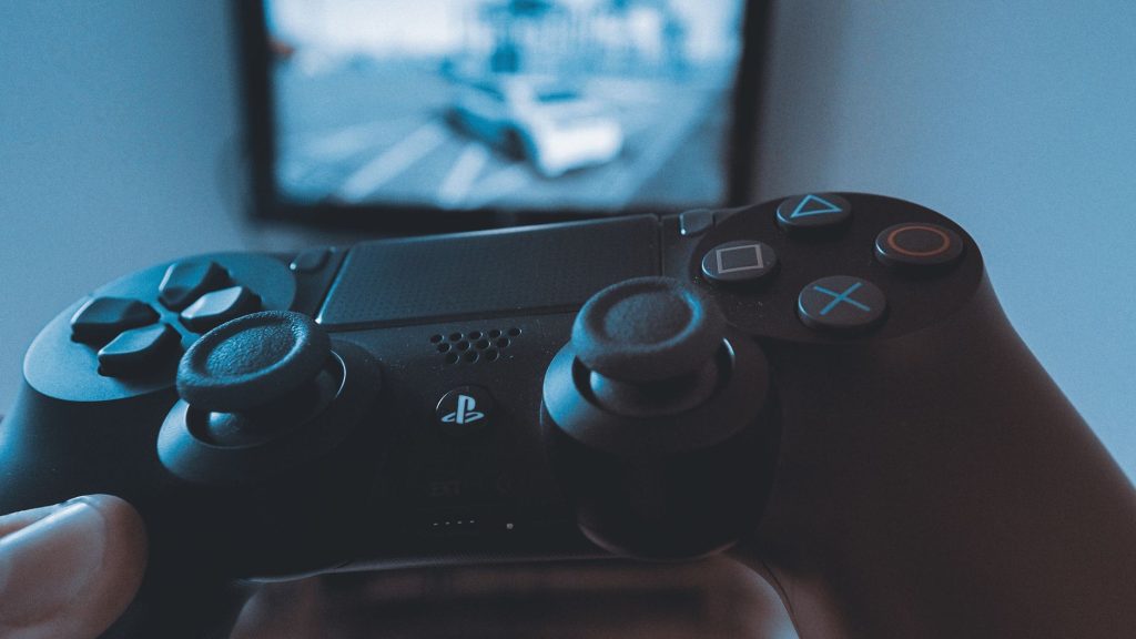 A hand holding a wireless game controller in front of a blurry screen, capturing the gaming experience. — Variables and Mutab