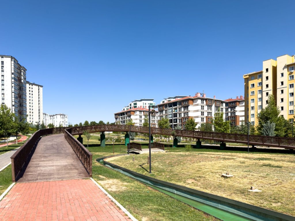 A sunny day in an urban park with modern buildings and a wooden bridge in Elâzığ, Türkiye. — What Are The Aspects To Be Cover