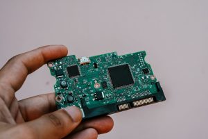 Close-up image of a hand holding a circuit board from a hard drive, showcasing electronic technology. — Why Go Outside When Y